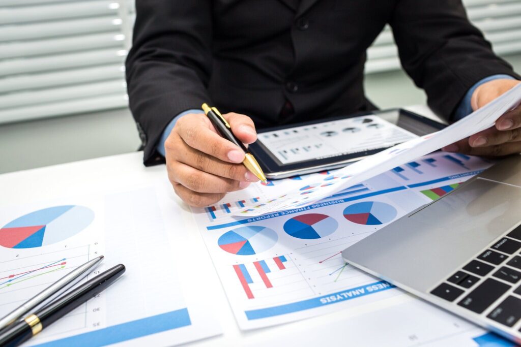 man holding pen examining charts and graphs with tablet on desk