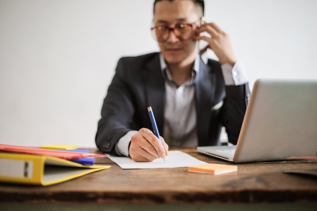 man at desk taking a phone call writing down notes