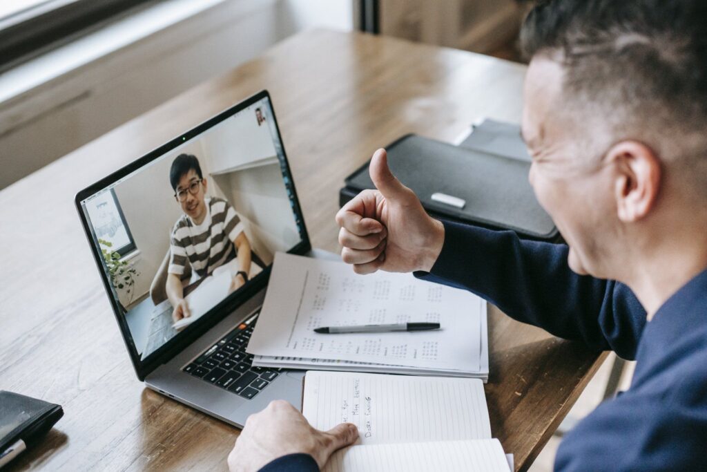 man giving thumbs up to person on video call laptop screen